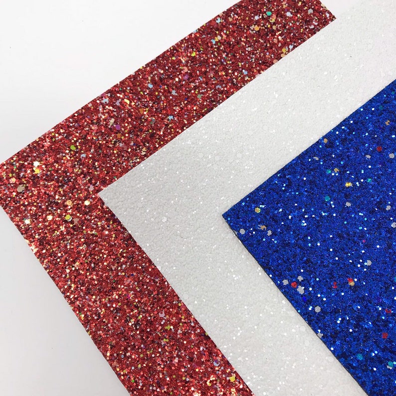 May include: Three sheets of glitter paper in red, white, and blue. The sheets are arranged in a triangle shape.