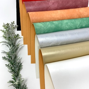 May include: A collection of eight different colored faux leather sheets. The sheets are rolled up and arranged in a row from darkest to lightest. The colors are black, red, burgundy, orange, green, silver, gold, and white.