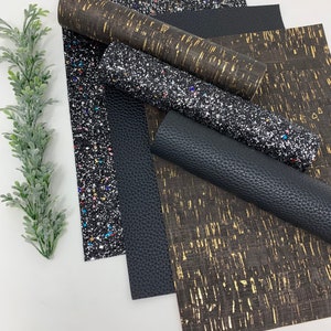 May include: A set of four different patterned fabric sheets. The sheets are black, gold, and silver with glitter. The sheets are arranged in a stack.