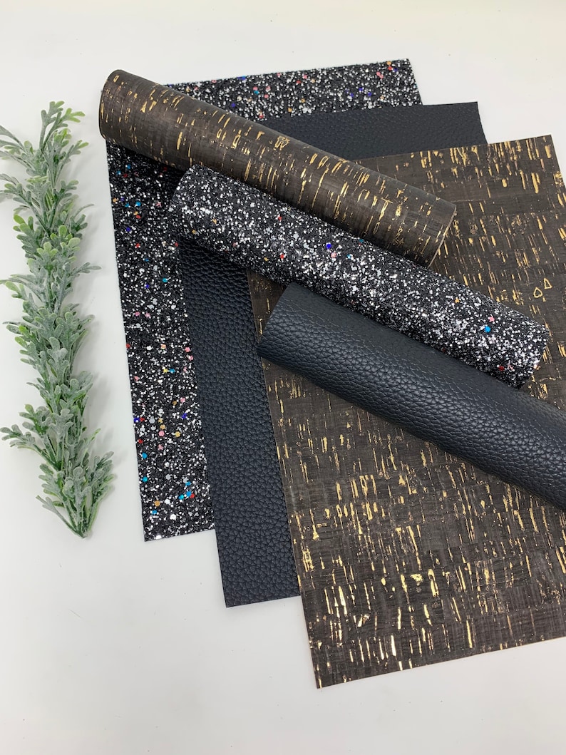 May include: A set of four different patterned fabric sheets. The sheets are black, gold, and silver with glitter. The sheets are arranged in a stack.