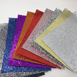 May include: A collection of ten glitter sheets in various colors, including black, silver, blue, purple, red, orange, pink, yellow, and white. The sheets are arranged in a fan shape, with the black sheet at the bottom and the white sheet at the top.