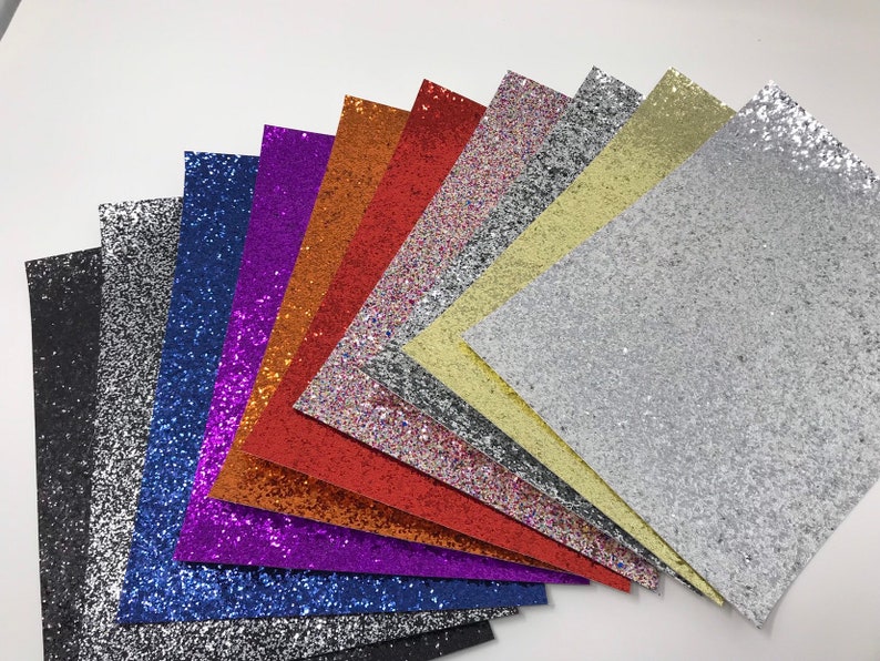 May include: A collection of ten glitter sheets in various colors, including black, silver, blue, purple, red, orange, pink, yellow, and white. The sheets are arranged in a fan shape, with the black sheet at the bottom and the white sheet at the top.