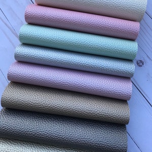 May include: A stack of eight different colored faux leather sheets. The sheets are arranged in a graduated color scheme from white to light pink to light green to light purple to brown to gray to beige.