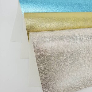 May include: Three sheets of textured metallic paper in turquoise, gold, and silver. The paper has a subtle embossed pattern.