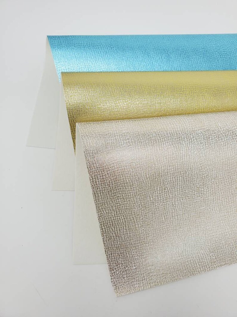 May include: Three sheets of textured metallic paper in turquoise, gold, and silver. The paper has a subtle embossed pattern.
