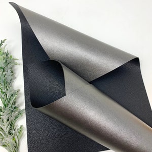 May include: A sheet of black faux leather with a silver metallic faux leather sheet folded on top. The silver sheet has a textured surface.