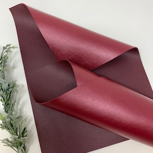May include: A sheet of burgundy faux leather with a smooth, shiny finish on one side and a textured, pebbled finish on the other side.