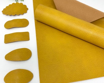 May include: A sheet of mustard yellow faux leather with a textured surface. Five pieces of the same faux leather are cut into different shapes, including a cloud, two rectangles, and two ovals.