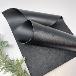 May include: Black faux leather sheet with a textured surface. The sheet is folded in half and the edges are visible.