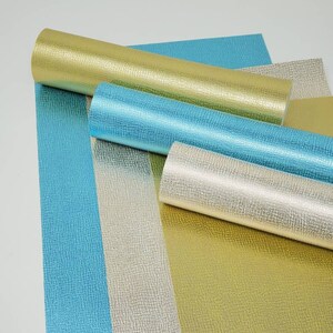 May include: Four rolls of metallic textured vinyl in gold, silver, and two shades of blue. The vinyl is rolled up and laid out on a white surface.
