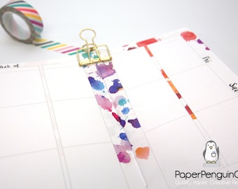 May include: A planner page with a gold binder clip and colorful watercolor washi tape. A roll of striped washi tape sits nearby. The planner page has a penguin logo and the text "PaperPenguinCo."