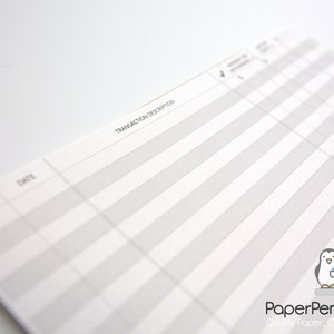 May include: Close-up of a white ledger book with gray striped columns and the words "Transaction Description" printed at the top. The PaperPenguinCo. logo is in the bottom right corner.