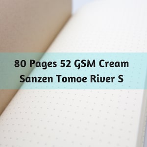 May include: Open notebook with cream-colored pages and a dotted pattern. The text on the image reads: "80 Pages 52 GSM Cream Sanzen Tomoe River S". The notebook is open to reveal the interior pages.