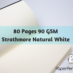 May include: Open notebook with dot grid pages. The text on the image reads: 80 Pages 90 GSM Strathmore Natural White. The notebook has a black spine and a light-colored paper. The Paper Penguin Co. logo is in the bottom right corner.