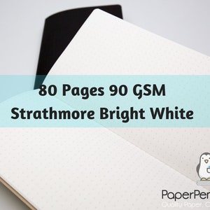 May include: Open notebook with 80 pages of Strathmore Bright White paper, 90 GSM, with a dot grid pattern. The notebook has a black cover and a light brown spine. The text "80 Pages 90 GSM Strathmore Bright White" is displayed.