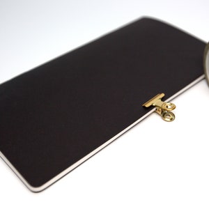 May include: A black notebook with a gold clip and a roll of gold and white chevron patterned washi tape. The notebook is open, and the clip is holding the pages together. The tape is partially unrolled.