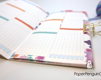 May include: Open planner with grid pages, colorful accents, and a gold binder clip. The pages have a grid pattern with colored rectangular highlights. A roll of patterned tape is visible in the background. The PaperPenguinCo logo is in the bottom right corner.