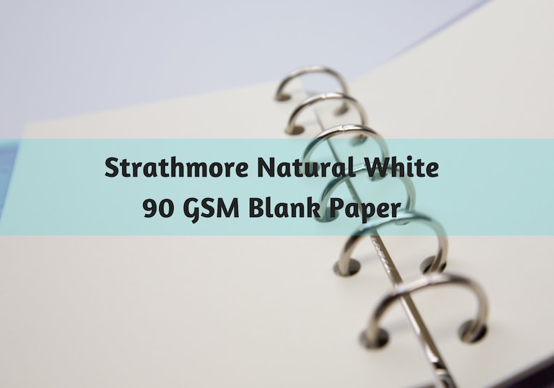 May include: Close-up of Strathmore Natural White 90 GSM blank paper in a binder. The paper is a bright white, and the binder rings are silver. The text is displayed on a light blue background.