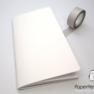 May include: An open, off-white notebook with blank pages, next to a roll of silver glitter tape. The notebook is on a white surface. The PaperPenguinCo. logo is in the bottom right corner.
