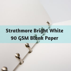 May include: Open notebook with bright white blank paper. The text "Strathmore Bright White 90 GSM Blank Paper" is displayed on a light blue background. The notebook has silver metal rings.