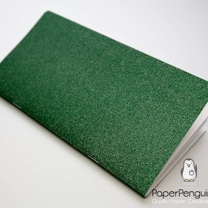 May include: A green notebook with a textured cover, open to reveal blank white pages. The notebook is rectangular and lies at an angle. The PaperPenguinCo logo is in the bottom right corner.
