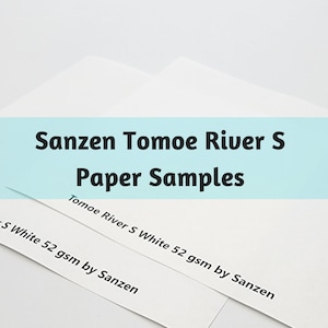 May include: Two white paper samples labeled "Sanzen Tomoe River S Paper Samples." The text "Tomoe River S White 52 gsm by Sanzen" is printed on the bottom of the samples. The background is white.