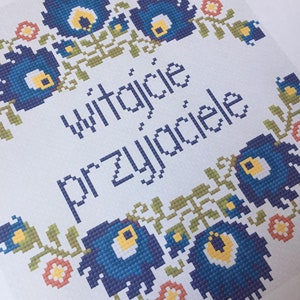 May include: A white card with a blue and yellow floral border. The text "witajcie przyjaciele" is written in the centre of the card.
