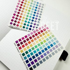 May include: Two sticker sheets with colorful dots and squares rest on a white dotted notebook. The stickers display a rainbow of colors, from pink and red to blue and gray. The text "CHIC STREET STICKER BOUTIQUE" is printed on the stickers.