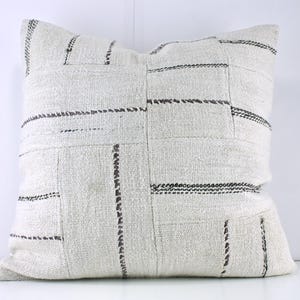 May include: White throw pillow with a geometric pattern of black and brown stitching. The pillow is made of a soft, woven fabric.