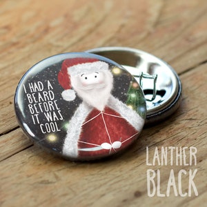 May include: A round button with a black background and a cartoon Santa Claus wearing a red and white suit. The text "I had a beard before it was cool" is written in white on the button.