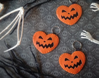 May include: Three orange felt heart-shaped keychains with black stitched details depicting jack-o'-lantern faces.
