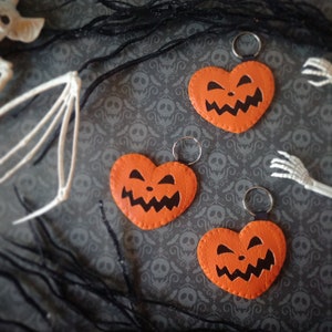 May include: Three orange felt heart-shaped keychains with black stitched details depicting jack-o'-lantern faces.