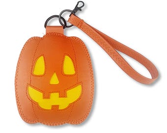 May include: An orange pumpkin-shaped keychain with a yellow cutout face featuring two triangular eyes, a triangular nose, and a jagged mouth. The keychain includes a matching orange wrist strap and a black metal lobster clasp and ring attachment.