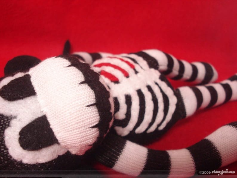 May include: A plush toy made from black and white striped fabric, featuring a white skeleton rib cage applique on the torso and a stitched face. The toy has long, striped limbs and a tail, with the text 2009 staceyjean.com visible at the bottom.