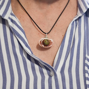 Puede incluir: Un collar de plata y cobre con un colgante de piedra verde en forma de concha.