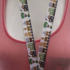 May include: A white lanyard with a repeating pattern of cartoon animals and train cars. The lanyard has a silver clip at the end.