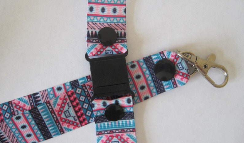 Pode incluir: Um cord&atilde;o colorido com um padr&atilde;o geom&eacute;trico em tons de rosa, azul e preto. O cord&atilde;o tem uma fivela preta e um gancho girat&oacute;rio prateado.