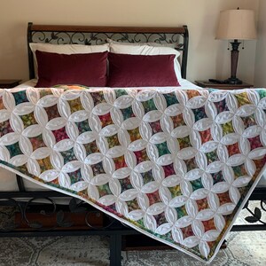 May include: A white quilt with a floral pattern in shades of green, red, and orange. The quilt is draped over a black metal bed frame.