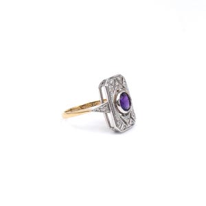 Peut inclure: Une bague rectangulaire vintage avec une monture dorée et un sertissage argenté. La bague présente une pierre précieuse ovale violette centrale, entourée de plus petites pierres précieuses claires. Le sertissage a un design Art Déco.