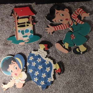 Peut inclure: D&eacute;coupes en bois vintage de personnages de dessins anim&eacute;s et d'un puits. Le gar&ccedil;on porte une chemise ray&eacute;e rouge et blanche et une salopette verte. La fille porte une robe bleue &agrave; motifs floraux blancs. Le puits a un toit rouge et une base turquoise.