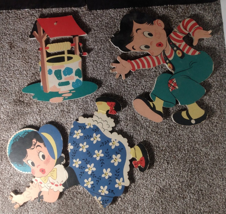 Peut inclure: D&eacute;coupes en bois vintage de personnages de dessins anim&eacute;s et d'un puits. Le gar&ccedil;on porte une chemise ray&eacute;e rouge et blanche et une salopette verte. La fille porte une robe bleue &agrave; motifs floraux blancs. Le puits a un toit rouge et une base turquoise.