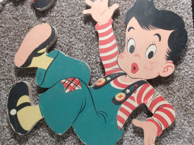 Peut inclure: Puzzle en bois vintage repr&eacute;sentant un gar&ccedil;on de dessin anim&eacute; en salopette turquoise et une chemise ray&eacute;e rouge et blanche. Le gar&ccedil;on a les cheveux noirs et les joues roses, un bras lev&eacute;. Les pi&egrave;ces du puzzle sont sur un tapis gris.