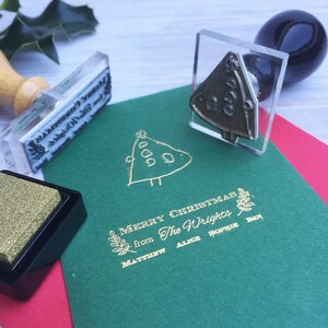May include: A set of three gold-colored rubber stamps on a green card. The stamps feature a Christmas tree, the text "Merry Christmas from The Wrights", and the names "Matthew, Alex, Sophie, Ben".