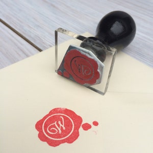 May include: A clear acrylic stamp with a red wax seal impression of the letter "W" inside a circle. The stamp is on a white surface with a red wax seal impression of the letter "W" inside a circle.