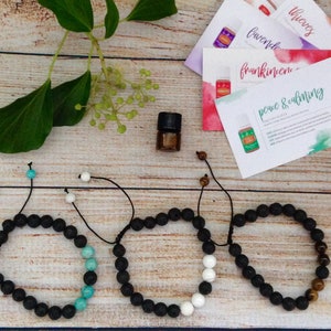 May include: Essential oil diffuser bracelets with black lava beads and accent beads in turquoise, white, and tiger's eye. A small essential oil bottle and cards with essential oil names are also present.