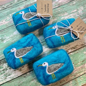 May include: Four blue felted soap bars with a seagull design. The soaps are wrapped in twine and have labels that read "Lavender Felted Soap" and "Mint & Eucalyptus Felted Soap".