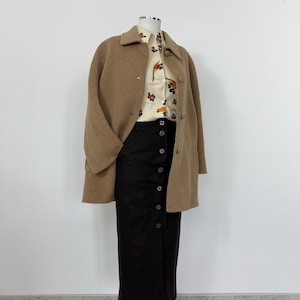 May include: A brown wool coat with a button closure and a brown skirt with a button front. The skirt is knee-length and the coat is mid-thigh length.