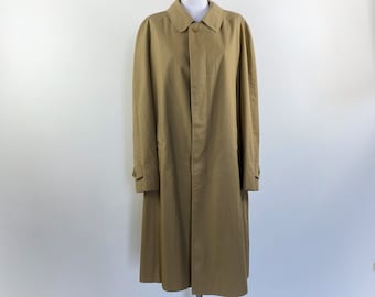 Op de afbeelding: Een beige trenchcoat op een paspop. De jas heeft een knoopsluiting, een kraag en lange mouwen. De jas is gemaakt van een gladde stof en heeft een knielange zoom. De jas heeft een neutrale kleur.