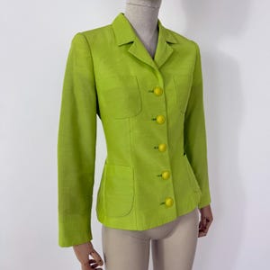 May include: A lime green blazer with a tailored fit. The blazer features a notched collar, two front pockets, and bright yellow buttons. The long-sleeved jacket is displayed on a mannequin.