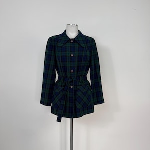 Könnte beinhalten: Eine grüne und schwarze karierte Jacke mit Knopfleiste und Gürtel. Die Jacke hat zwei große Taschen auf der Vorderseite.